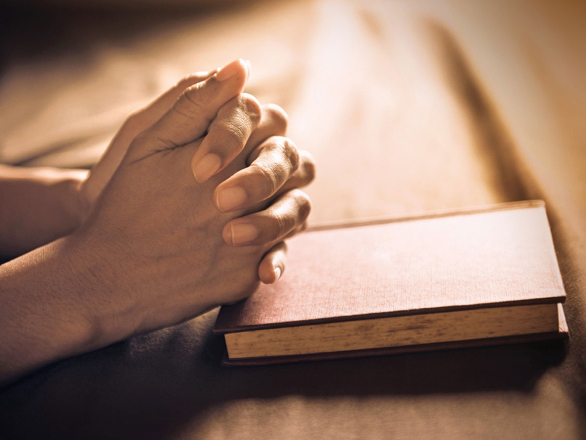 hands praying on bible